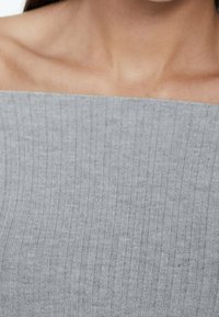 Zbliżenie na szyję i ramiona osoby noszącej jasnoszary, prążkowany top na ramiączkach.