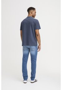 Navy blue cotton t-shirt with short sleeves, paired with light blue denim jeans featuring a slight fade and back pockets; casual footwear included.
