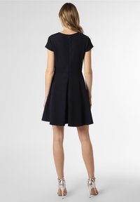 Marinblå klänning med korta ärmar, utsvängd kjol, strukturerad tyg, dragkedja bak och silverfärgade högklackade sandaler.