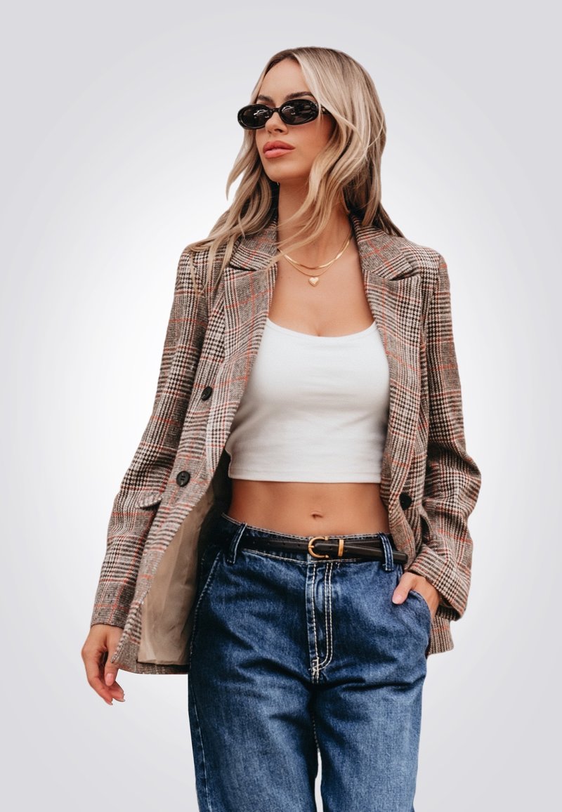 Blazer à carreaux dans les couleurs marron, rouge et crème ; double boutonnage avec deux boutons ; associé à un crop top blanc et un jean bleu taille haute.