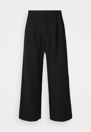 Pantaloni neri a gamba larga con una texture liscia, frontale plissettato, vita elasticizzata e chiusura con un singolo bottone.