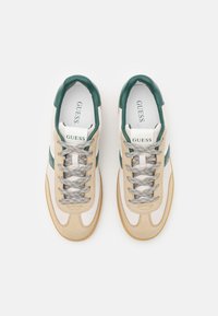 Beige and white sneakers with green accents, suede and fabric materials, round toe, textured laces, branded tongue, and gum rubber sole.