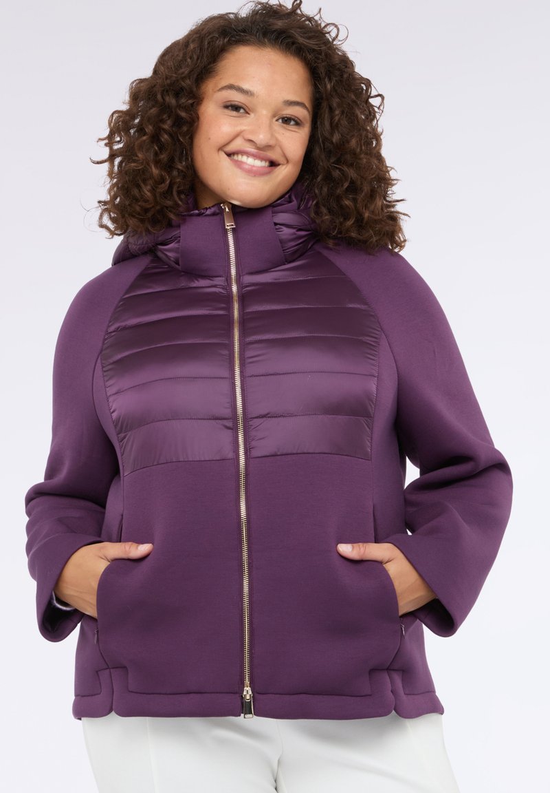 Chaqueta con capucha morada con un panel frontal acolchado, cierre de cremallera y bolsillos laterales. Presenta una tela suave y un ajuste relajado.