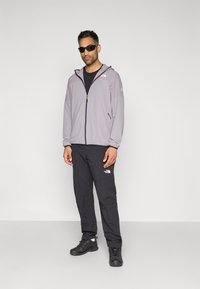 Ανοιχτό γκρι ζακέτα με φερμουάρ και κουκούλα, μαύρο μπλουζάκι, μαύρο παντελόνι με λογότυπο, μαύρα αθλητικά παπούτσια και γυαλιά ηλίου. Απλή, λειτουργική εξωτερική ενδυμασία.