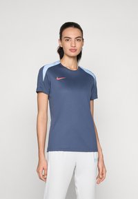 Navy athletic shirt with light blue shoulder accents and a red Nike logo. Made of textured fabric, featuring a round neck and short sleeves.
