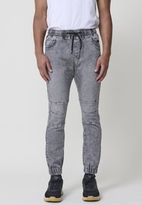 Pantalones jogger de mezclilla gris con cintura elástica, cierre de cordón y piernas ajustadas que presentan detalles en los paneles de las rodillas y puños.