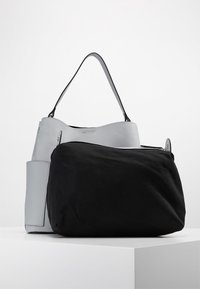 Sac en cuir gris avec un fond en tissu noir, doté d'une seule poignée et d'une forme douce et arrondie. Notable pour ses matériaux contrastés.