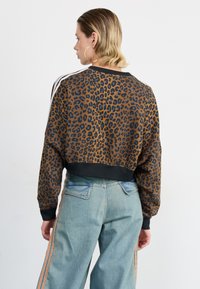 Braun gepunkteter, kurzer Sweatshirt mit schwarzem Rippenbund, weißen Schulterstreifen und entspannter Passform, kombiniert mit hellblauen weiten Jeans.