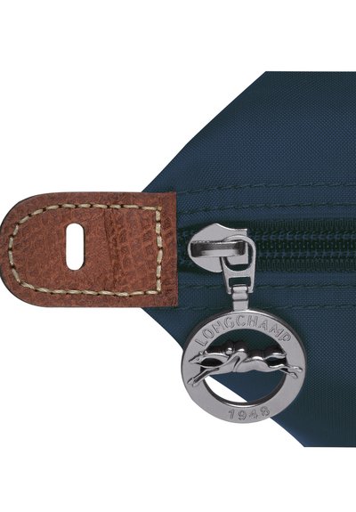 Navy blue fabric pouch with a brown leather zipper pull, featuring a round silver logo tag with a running horse and "LONGCHAMP 1948" inscription.
