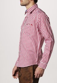 Rood-wit geruit overhemd met knopen en een kraag, voorzien van een borstzak en een lichte textuur, gedragen met een bruine broek.