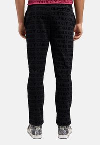 Sorte træningsbukser med præget logo mønster, slim fit, elastisk talje og baglomme. Kombineret med mønstrede sneakers.