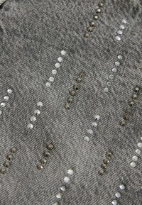 Denim w kolorze szarym z teksturowanym splotem. Zawiera rzędy błyszczących cekinów w kolorze białym, srebrnym i ciemnoszarym, ułożonych w ukośny wzór.