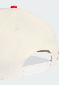 Gorra de color crema con un botón superior rojo, textura suave, correa blanca ajustable en la parte de atrás y agujeros de ventilación a los lados.