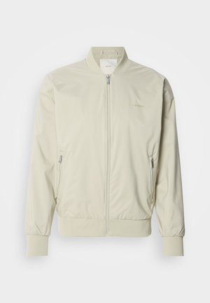 Light beige bomber jacket made of smooth, lightweight material. Features a zip front, ribbed cuffs, and side pockets. Subtle logo detail.