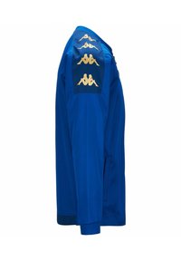 Chaqueta deportiva azul con un logo dorado en el panel negro, con cremallera frontal y puños acanalados. Textura suave con un diseño ajustado.