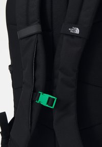 Black backpack with padded straps, featuring a green plastic buckle and a small white logo. The material appears durable and textured.