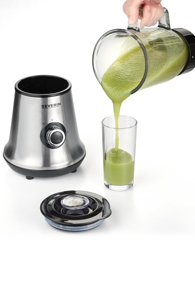 Edelstahlmixer mit einem glatten, konischen Fuß, einer Glaskanne, die einen grünen Smoothie in ein klares Glas gießt, schwarzen Deckel am Boden.