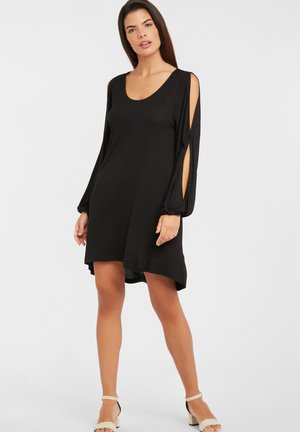 Schwarzes Kleid mit langen Ärmeln, mit Ausschnitten an den Schultern, einem Rundhalsausschnitt und asymmetrischem Saum. Weiche Stofftextur.