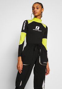 Svart långärmad topp med neongula detaljer och logotyp, tillsammans med svarta cargobyxor med reflexdetaljer och flera fickor.