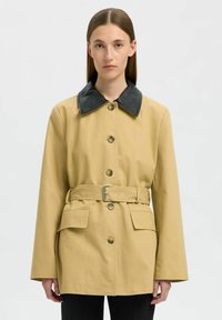 Cappotto beige con colletto in pelle nera, bottoni frontali, vita con cintura e due tasche; tessuto testurizzato con vestibilità comoda.