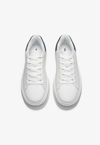 Hvite sneakers med overdel i glatt skinn, rund tå og flate snøringer. Har en svart detalj på hælen og strukturert gummisåle.