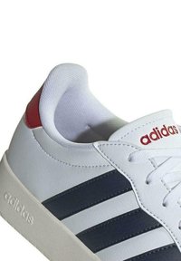 Sneaker sintetica bianca con strisce navy e accenti rossi. Presenta una punta rotonda, un design con lacci e un collare imbottito per il comfort.