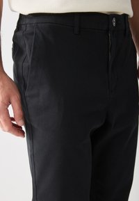 Black trousers featuring a zip fly, button closure, and side pockets. The fabric has a smooth texture with a tailored fit appearance.