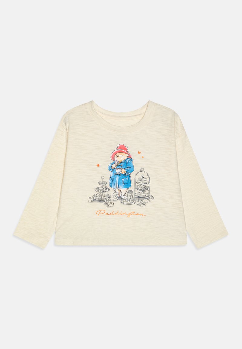 Bela majica s dolgimi rokavi iz bombaža, ki prikazuje risanega medvedka v modrem plašču in rdeči kapi, obkroženega s hrano ter besedilom "Paddington".