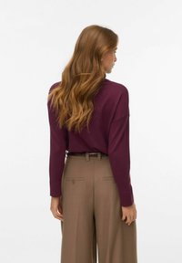 Maglietta a maniche lunghe bordeaux con una vestibilità rilassata, abbinata a pantaloni larghi a vita alta di colore marrone chiaro con tasche posteriori e una cintura.