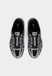 Ζευγάρι μαύρα και ασημί αθλητικά παπούτσια Nike με ανακλαστικές λεπτομέρειες και το λογότυπο "NIKE" στη γλώσσα, σε θέαση από πάνω σε λευκό φόντο.