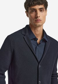 Marine cardigan med tekstureret strik, med sjalskrave og knaplukning, båret over en matchende skjorte med knapper.