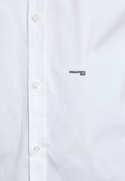 Chemise blanche à boutons fabriquée en tissu lisse avec un col pointu. Présente un petit logo noir "DSQUARED2 1995" sur la zone gauche de la poitrine.