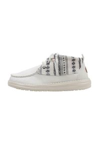 Zapatillas blancas casuales con un upper de tela estampada, suela texturizada en color crema y diseños geométricos en negro contrastante en el cuello.