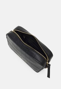 Černá kabelka z umělé kůže s krokodýlím texture, se zlatými zipy a hladkým interiérem. Design je obdélníkový s horním zipem.