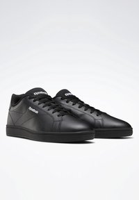Černé kožené tenisky s hladkou texturou, kulatou špičkou a tónovaným šitím. Obsahují černé tkaničky a bílé logo Reebok na boku.