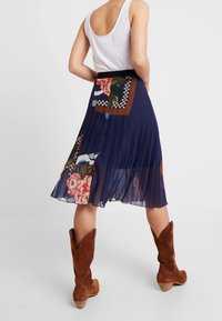 Námořnická plisovaná sukně s květinovým vzorem, doplněná vyšíváním, v kombinaci s hnědými semišovými kovbojskými botami. Hladká struktura látky, pružný pas.