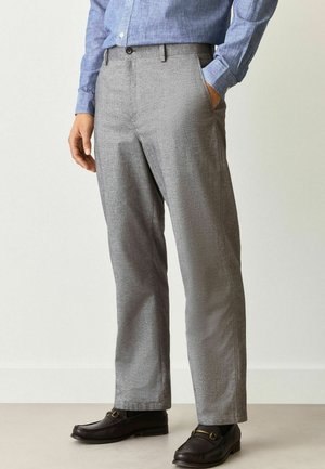 Graue Hose mit einem sanften Hahnentrittmuster, gerader Schnitt, Seitentaschen und einer glatten Stofftextur, kombiniert mit braunen Loafers.