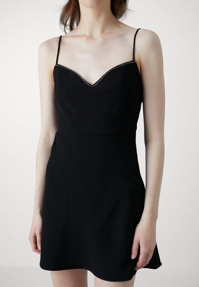Robe noire avec un corsage ajusté et une jupe évasée. Dotée de fines bretelles et d'un décolleté en V orné de clous métalliques. Texture lisse.