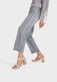 Sandali con tacco block a strappo, con una leggera lucentezza e un tacco glitterato texturizzato. Abbinati a jeans cropped blu chiaro con orli sfrangiati.