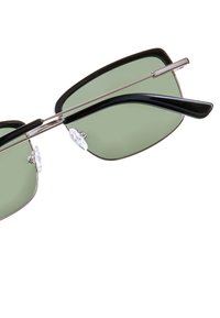 Sunglasses med gröna linser, svart plastbåge och silverfärgade metallinslag. Har näskuddar och en snygg, vass design.