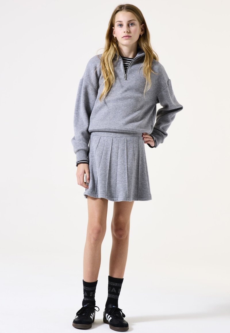 Grijze sweatshirt met een halve rits kraag, gecombineerd met een geplooide grijze rok. Zwarte sokken en zwarte schoenen met witte strepen. Eenvoudig en casual ontwerp.