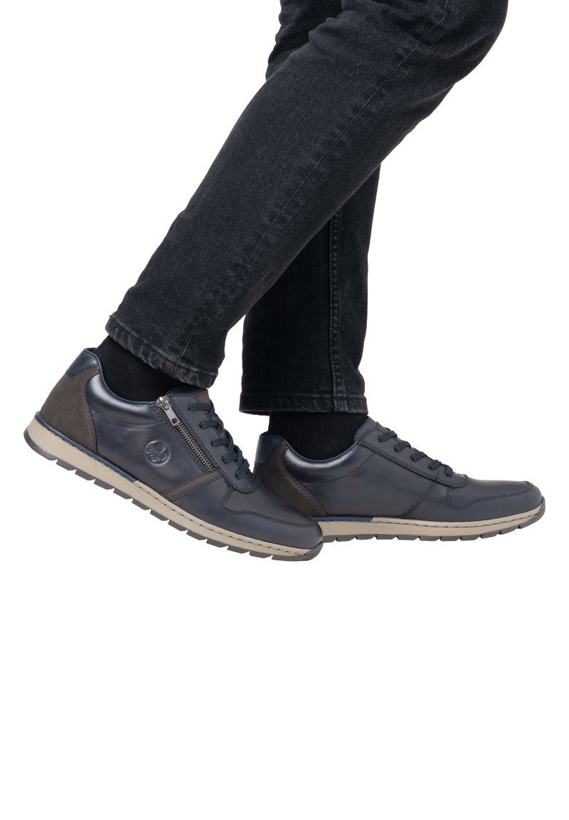 Baskets en cuir bleu marine pour hommes avec des accents texturés marron foncé, des fermetures à lacets et à zip, et une semelle en caoutchouc beige.