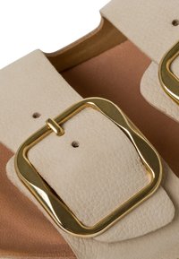 sandale en cuir beige avec deux larges lanières et boucles dorées, surface texturée et doublure intérieure marron.