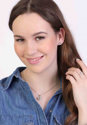 Zilveren hartvormige ketting, stud oorbellen en een ring, allemaal met een gepolijste afwerking; model draagt een denim shirt.