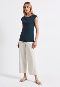 Top blu navy a maniche corte con scollatura rotonda e dettaglio a occhio di chiave, abbinato a pantaloni chiari a gamba larga e sandali neri con cinturini.