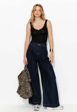 Débardeur noir avec dentelle, jean en denim foncé taille haute et large, sac tote à imprimé léopard et baskets argentées. Design simple et épuré.