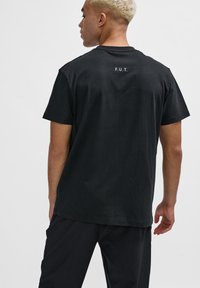 Schwarzes Baumwoll-T-Shirt mit kurzen Ärmeln, mit dem Text "F.U.T." in Weiß auf der oberen Rückseite. Einfaches Design und reguläre Passform.
