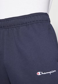 Navy blue sweatpants with an elastic waistband, side pockets, and a white embroidered "Champion" logo on the left thigh.