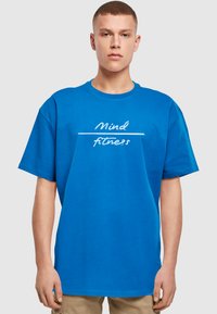 Blå bomulds T-shirt med korte ærmer og rund hals. Forsiden viser hvid tekst: "Mind fitness" med en vandret linje.