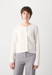 Strikket cardigan i hvitt med et teksturert sikksakk-mønster, rund hals, bølget kant og store, runde knapper foran.